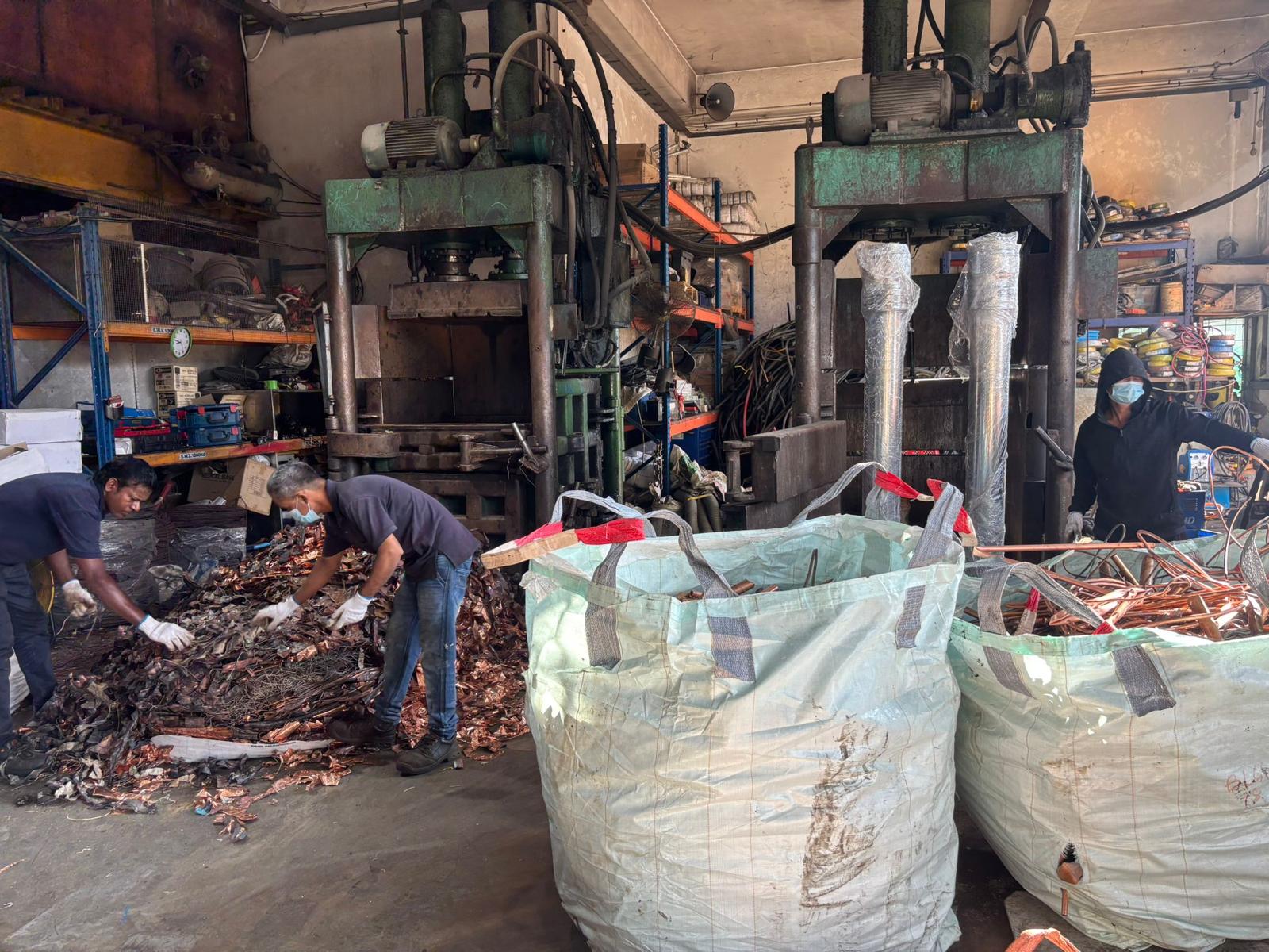Ogoo Recycle staff hand-sorting scrap copper by grade beside hydraulic baling presses at the Tuas yard